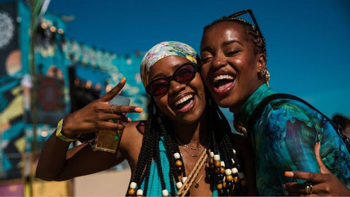 Two beautiful Nigerian ladies with smiles pose for a selfie at a vibrant Detty December celebration.