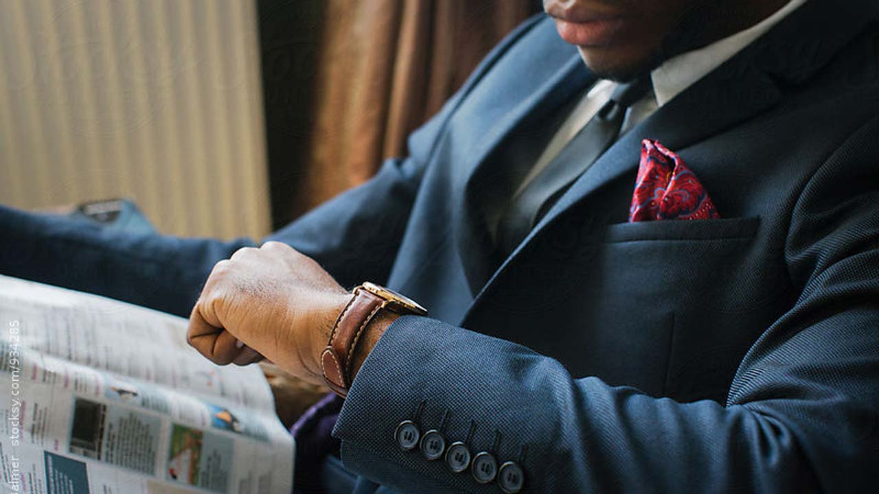 A Nigerian man in a suit looking at his wristwatch.
