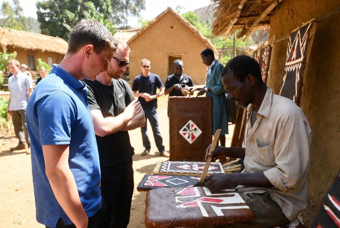 International tourists interact with an Imigongo artist in a Rwandan village.
