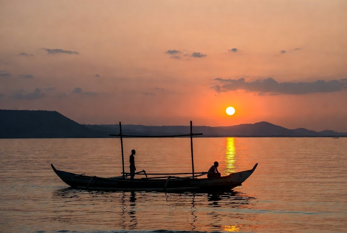 Lake Victoria at sunset with a traditional wooden fishing boat and silhouetted figures