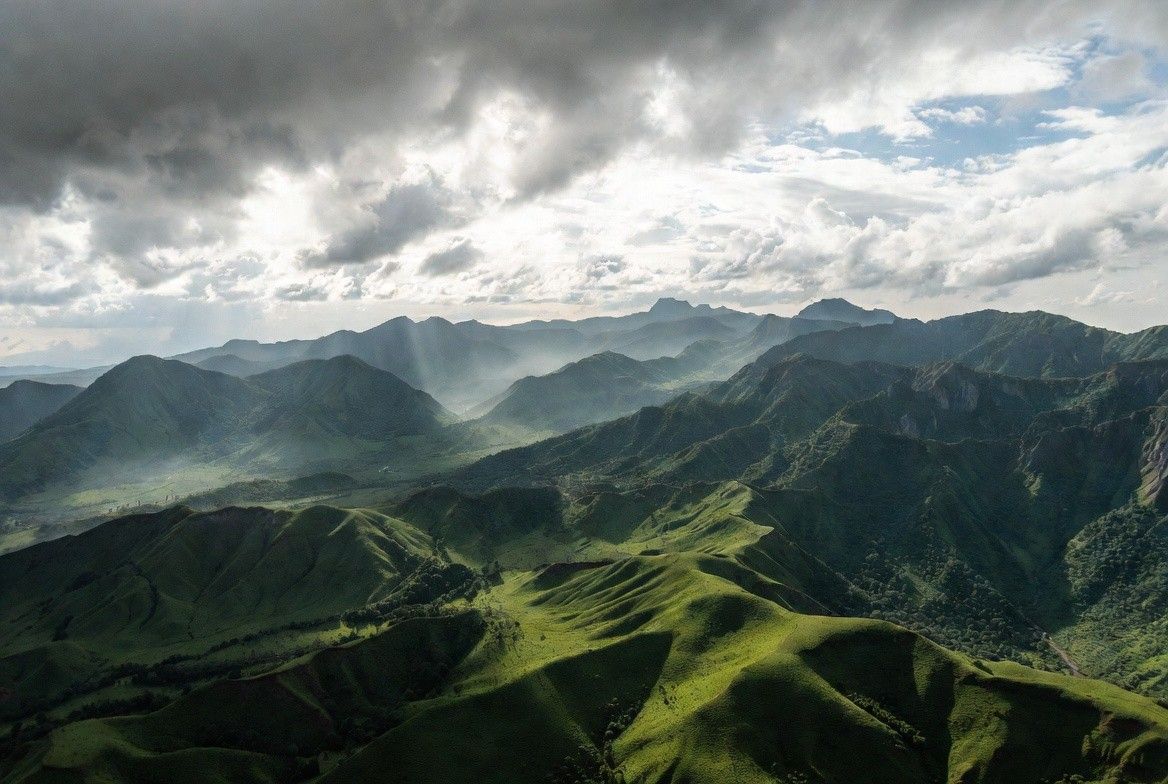 An aerial shot of the Virunga volcanic landscape, showing the layered green hills and volcanic peaks