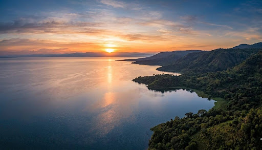 Aerial shot of Lake Albert at sunrise, wide, cinematic, water catching morning light with forested banks visible